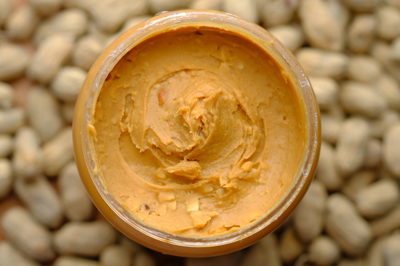Close-up of creamy peanut butter in a glass jar surrounded by peanuts. Tasty and homemade.